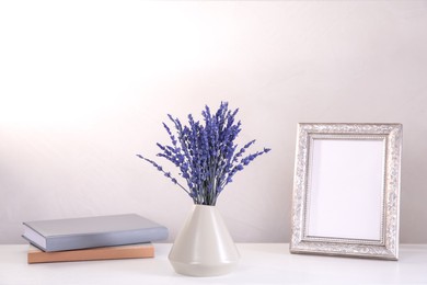 Bouquet of beautiful preserved lavender flowers, notebooks and blank photo frame on white table near beige wall