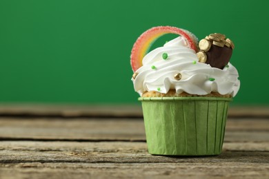 St. Patrick's day party. Tasty cupcake with sour rainbow belt and pot of gold toppers on wooden table, closeup. Space for text