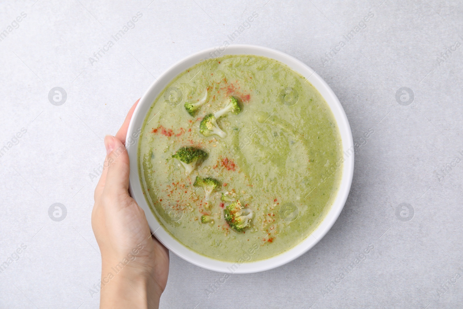 Photo of Woman with bowl of delicious broccoli cream soup at table, top view