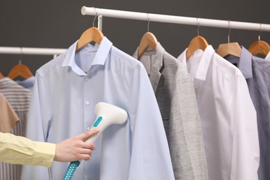 Woman steaming shirt on hanger in room, closeup
