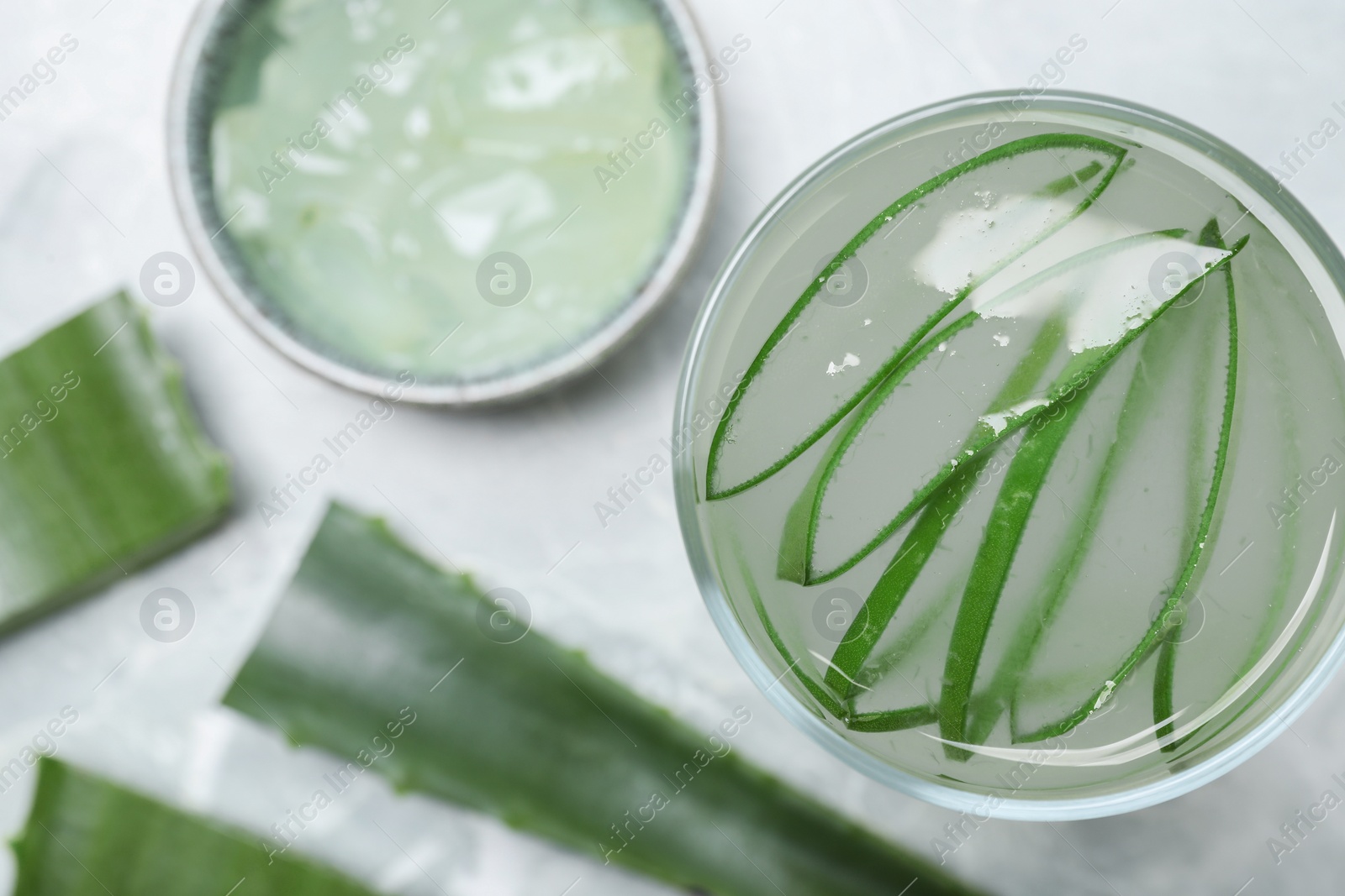 Photo of Tasty aloe juice in glass and cut fresh leaves on light grey table, flat lay