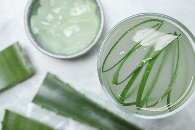 Photo of Tasty aloe juice in glass and cut fresh leaves on light grey table, flat lay