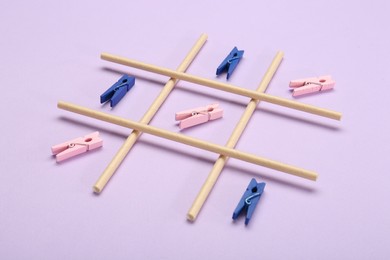 Photo of Tic tac toe game made with clothespins on lilac background