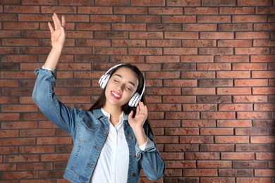 Photo of Beautiful young woman listening to music with headphones against brick wall. Space for text