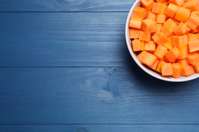 Photo of Bowl of fresh diced carrot on blue wooden table, top view. Space for text