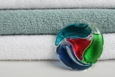 Laundry capsule and towels on white table, closeup. Space for text