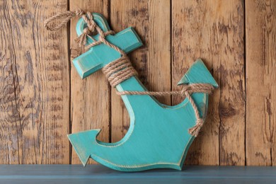 Photo of Anchor with hemp rope on light blue table near wooden wall