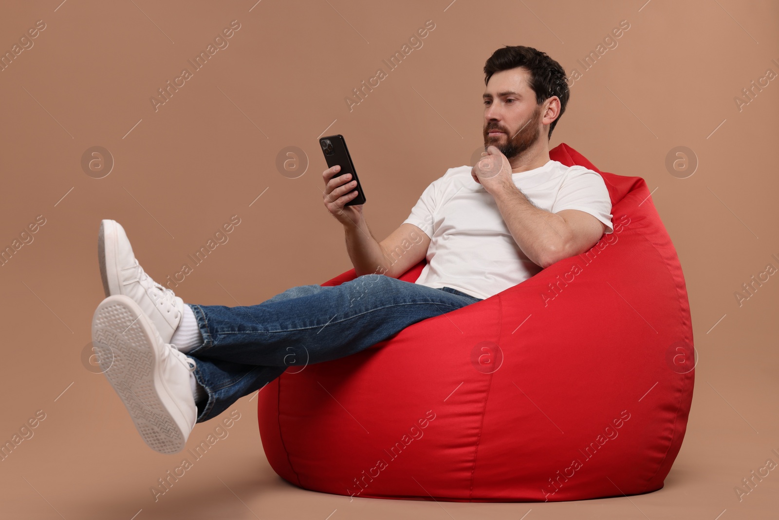 Photo of Handsome man with smartphone sitting on bean bag against light brown background