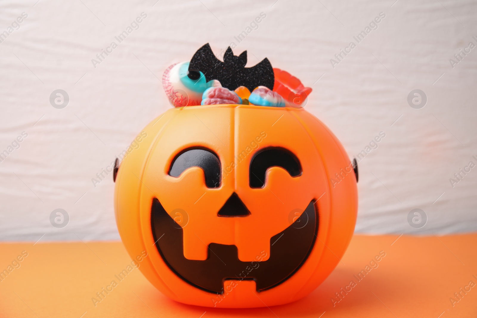 Photo of Halloween trick or treat bucket with different sweets on orange table