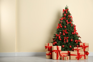 Decorated Christmas tree and gift boxes near beige wall. Space for text