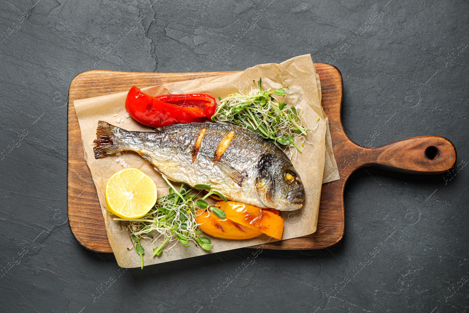 Photo of Delicious roasted fish and vegetables on dark grey table, top view