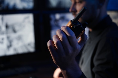 Male security guard with portable transmitter monitoring modern CCTV cameras indoors, closeup