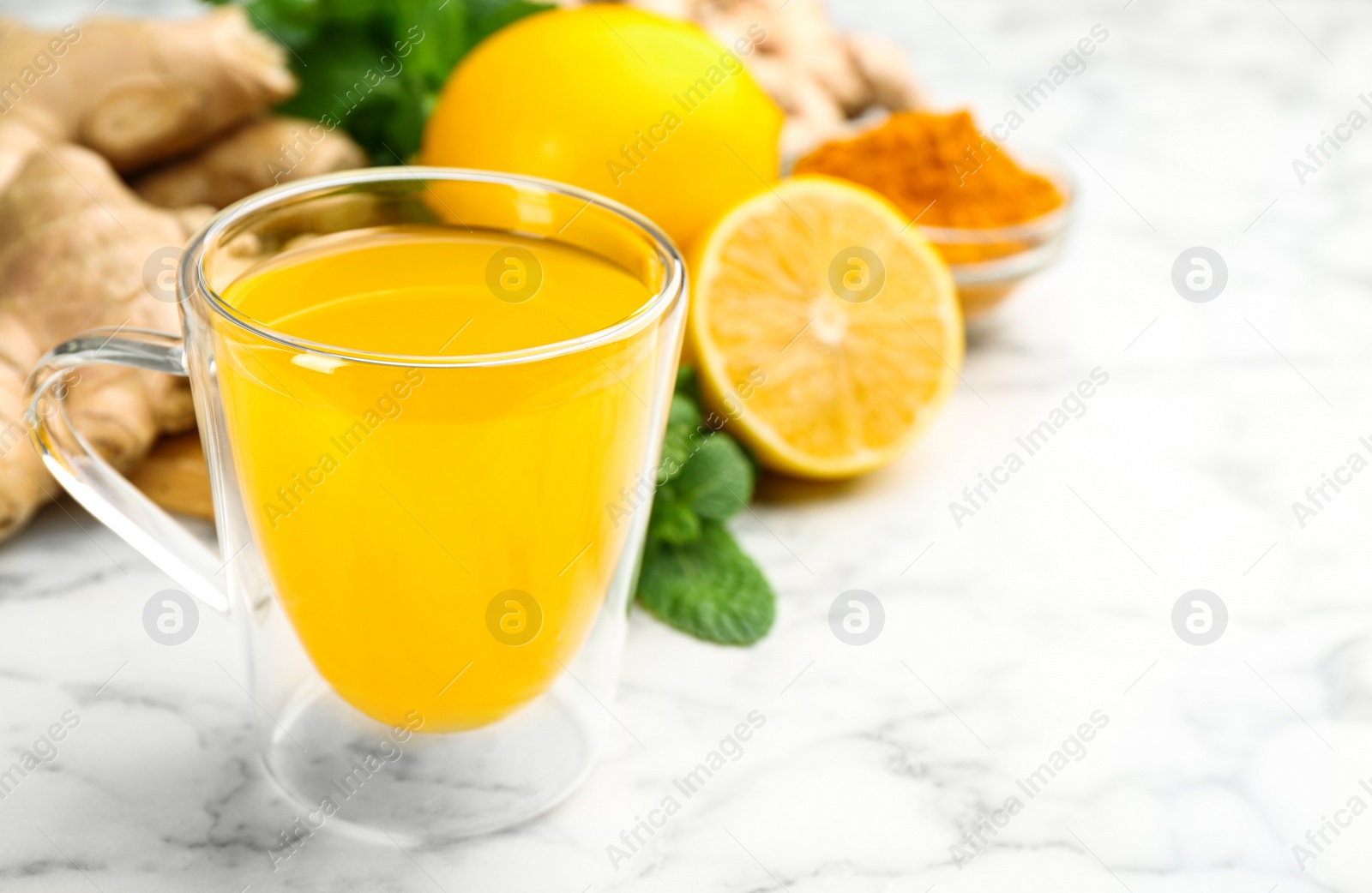 Photo of Immunity boosting drink and ingredients on white marble table, closeup. Space for text