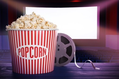 Image of Delicious popcorn and movie reel on blue wooden table in cinema, space for text