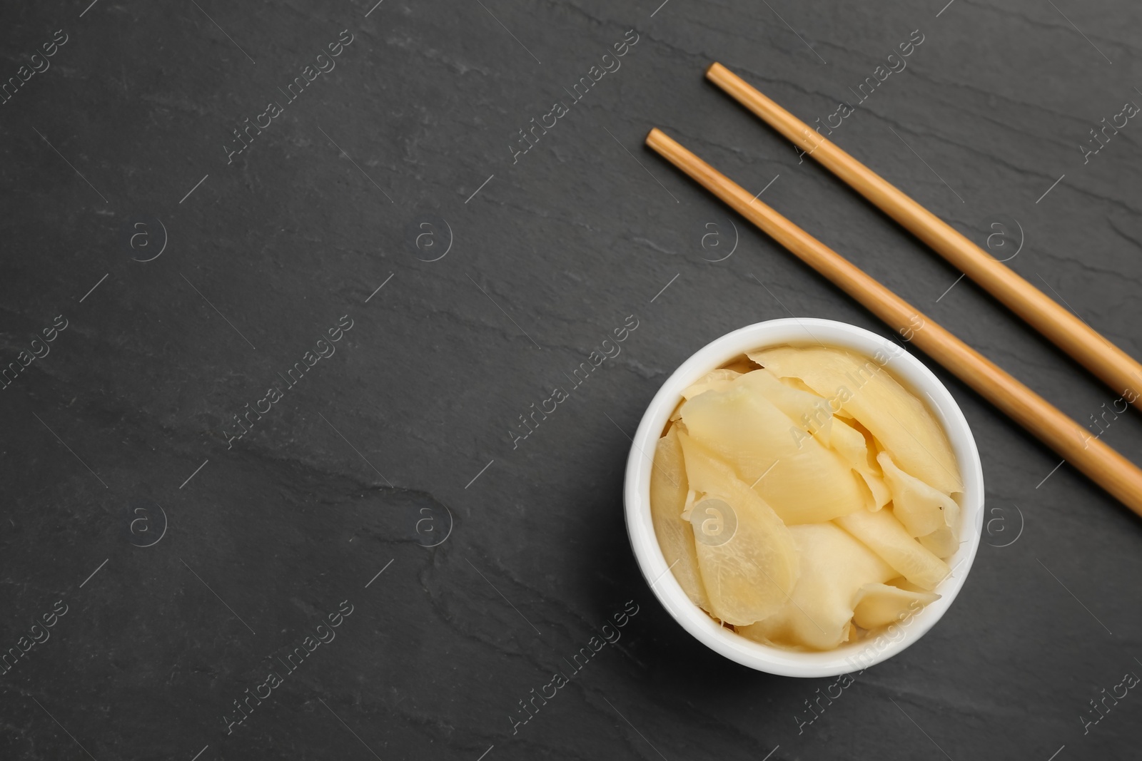 Photo of Pickled ginger in bowl and chopsticks on black table, flat lay. Space for text