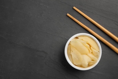 Photo of Pickled ginger in bowl and chopsticks on black table, flat lay. Space for text