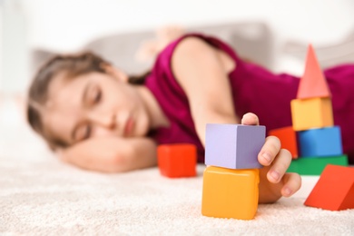Photo of Little girl with autistic disorder playing at home, closeup of cubes
