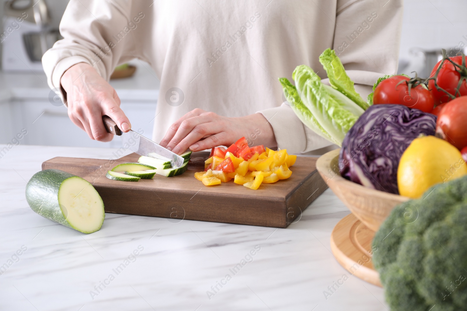 Photo of Woman cutting fresh vegetables at table in kitchen, closeup