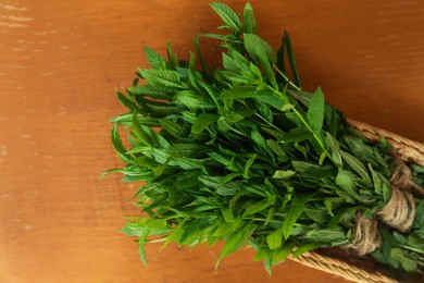 Photo of Bunches of beautiful green mint in wicker basket on brown wooden table, top view