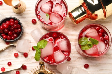 Tasty cranberry cocktail with ice cubes in glasses and bartender's tools on wooden table, flat lay