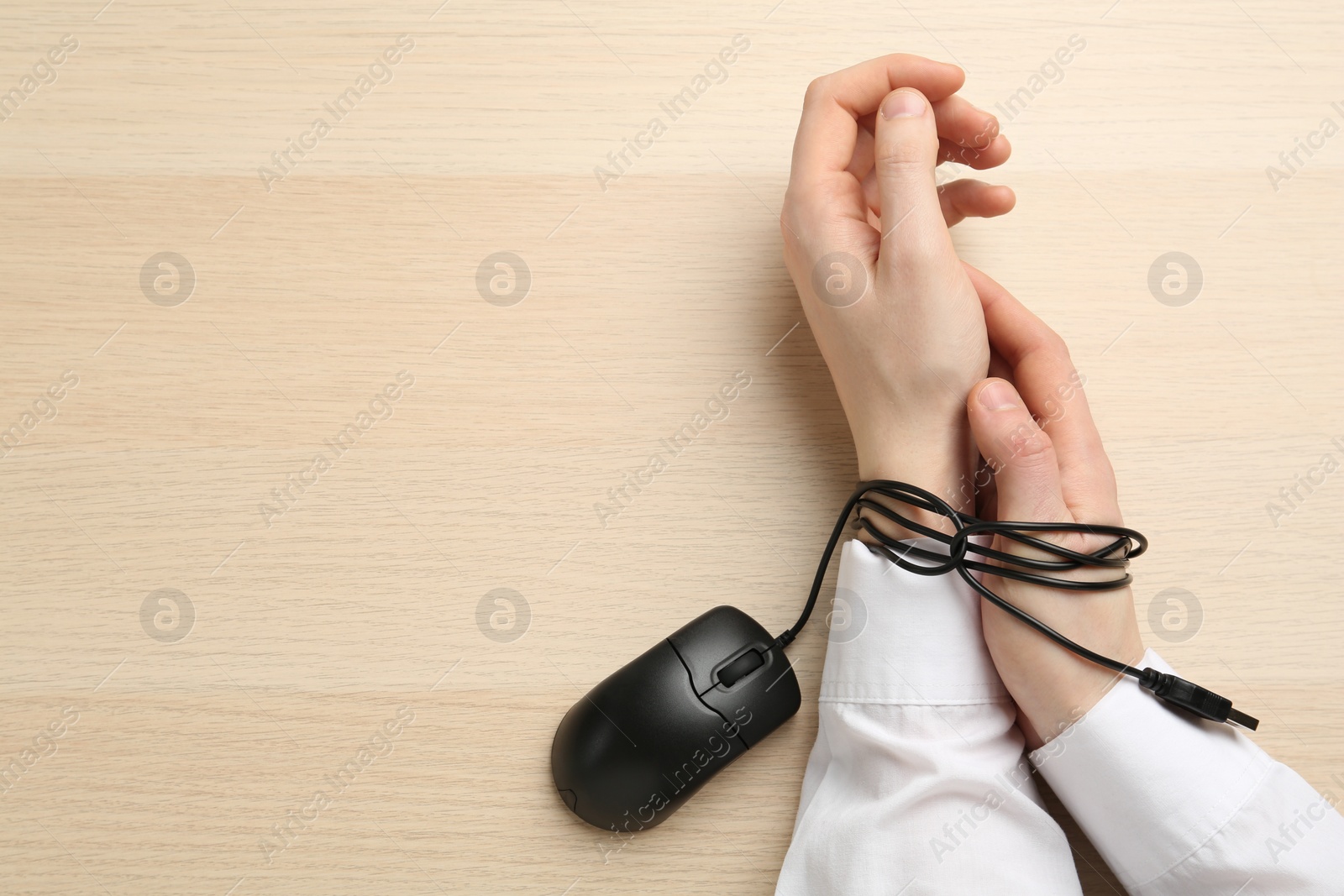 Photo of Man showing hands tied with computer mouse cable at wooden table, top view. Internet addiction