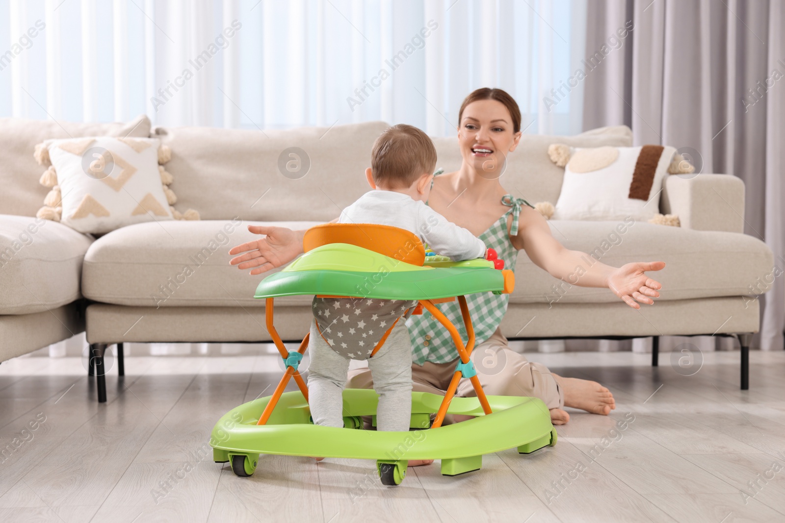 Photo of Little boy in baby walker hurrying to happy mother at home. Woman calling child with open arms