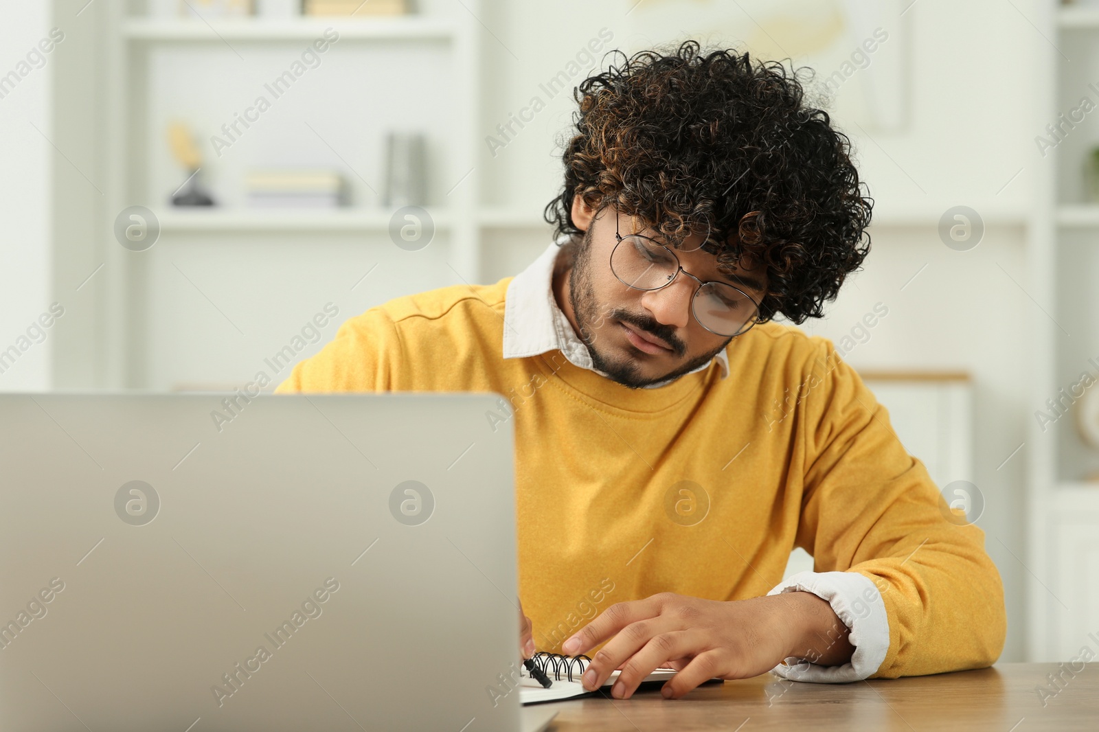 Photo of Handsome man taking notes near laptop in room