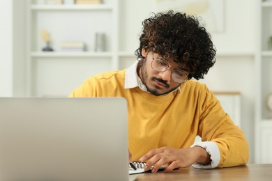 Handsome man taking notes near laptop in room