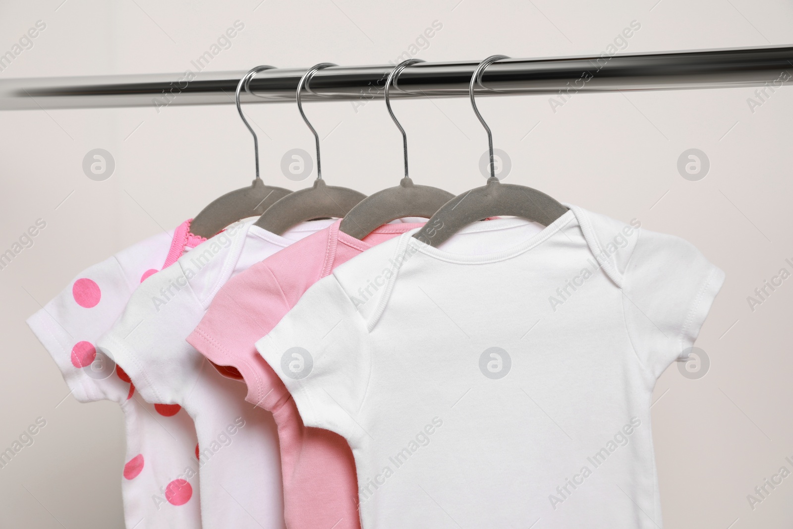 Photo of Baby bodysuits hanging on rack near white wall, closeup