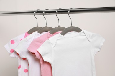 Baby bodysuits hanging on rack near white wall, closeup