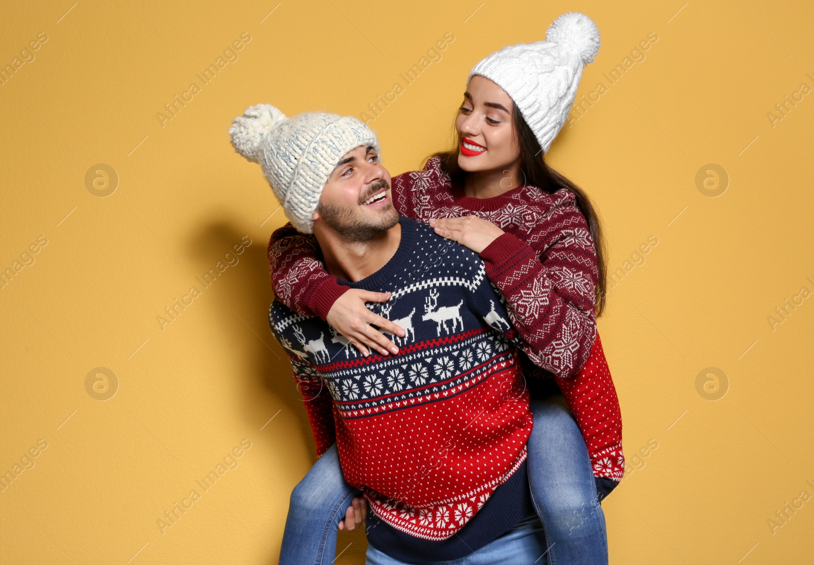 Photo of Young couple in warm sweaters and knitted hats on color background. Christmas celebration