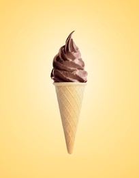 Delicious soft serve chocolate ice cream in crispy cone on pastel golden background