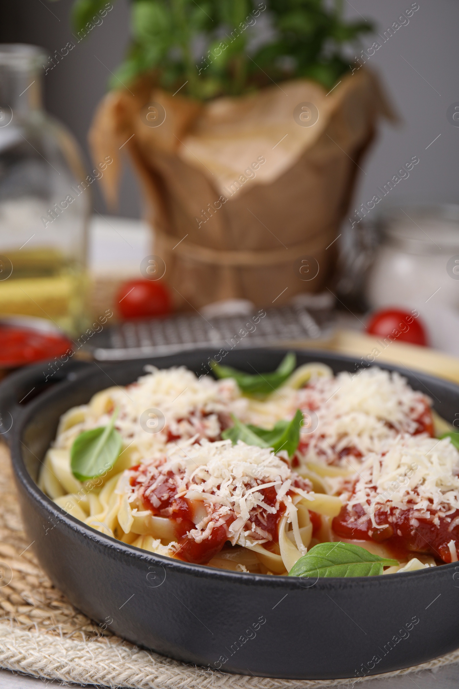 Photo of Delicious pasta with tomato sauce, basil and parmesan cheese on wicker mat, closeup