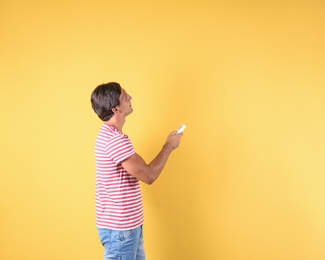 Photo of Young man with air conditioner remote on color background, copy space text