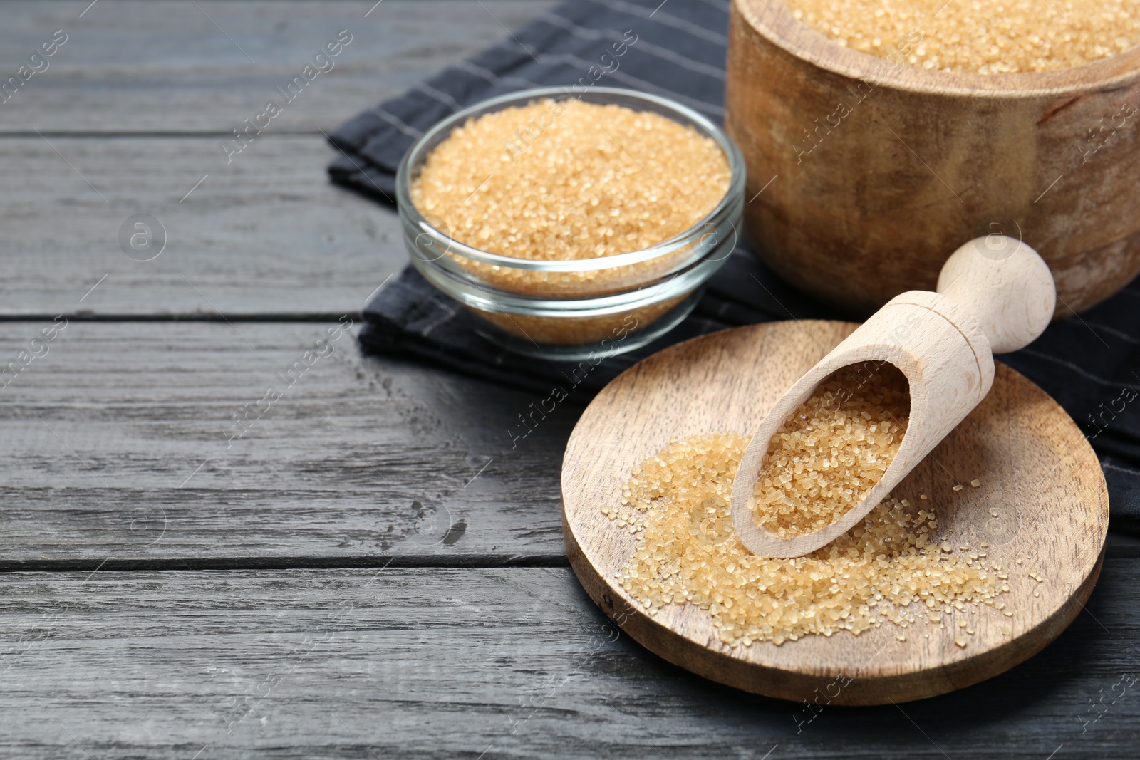 Photo of Brown sugar in bowls and scoop on black wooden table. Space for text