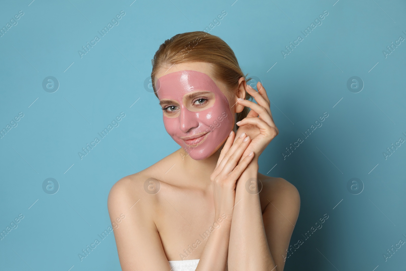 Photo of Young woman with pomegranate face mask on light blue background