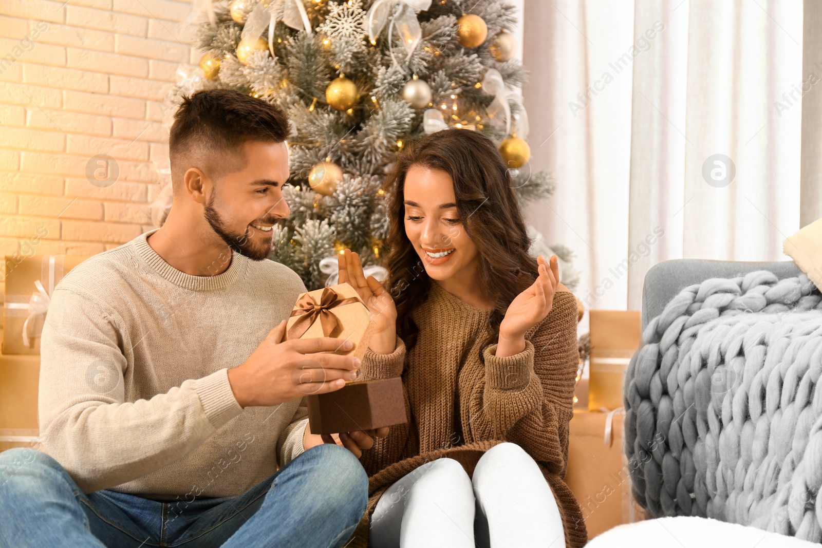 Image of Young man presenting Christmas gift to his girlfriend at home