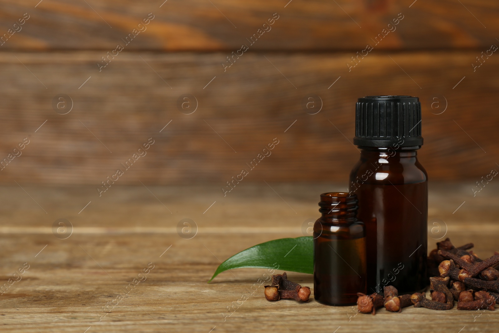 Photo of Essential oil, dried cloves and leaf on wooden table. Space for text
