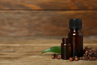 Essential oil, dried cloves and leaf on wooden table. Space for text