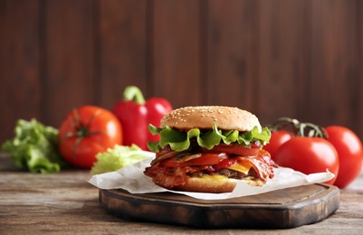 Tasty burger with bacon on wooden table. Space for text