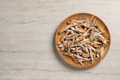 Photo of Plate of tasty dried anchovies on light wooden table, top view. Space for text