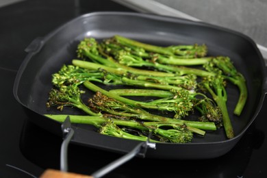 Photo of Grill pan with tasty cooked broccolini on cooktop, closeup