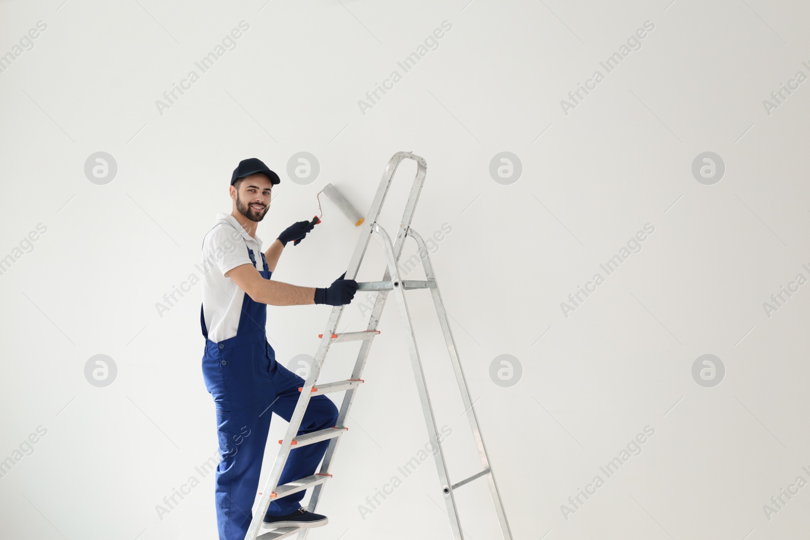 Photo of Handyman painting wall with roller brush indoors, space for text. Professional construction tools