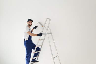 Photo of Handyman painting wall with roller brush indoors, space for text. Professional construction tools