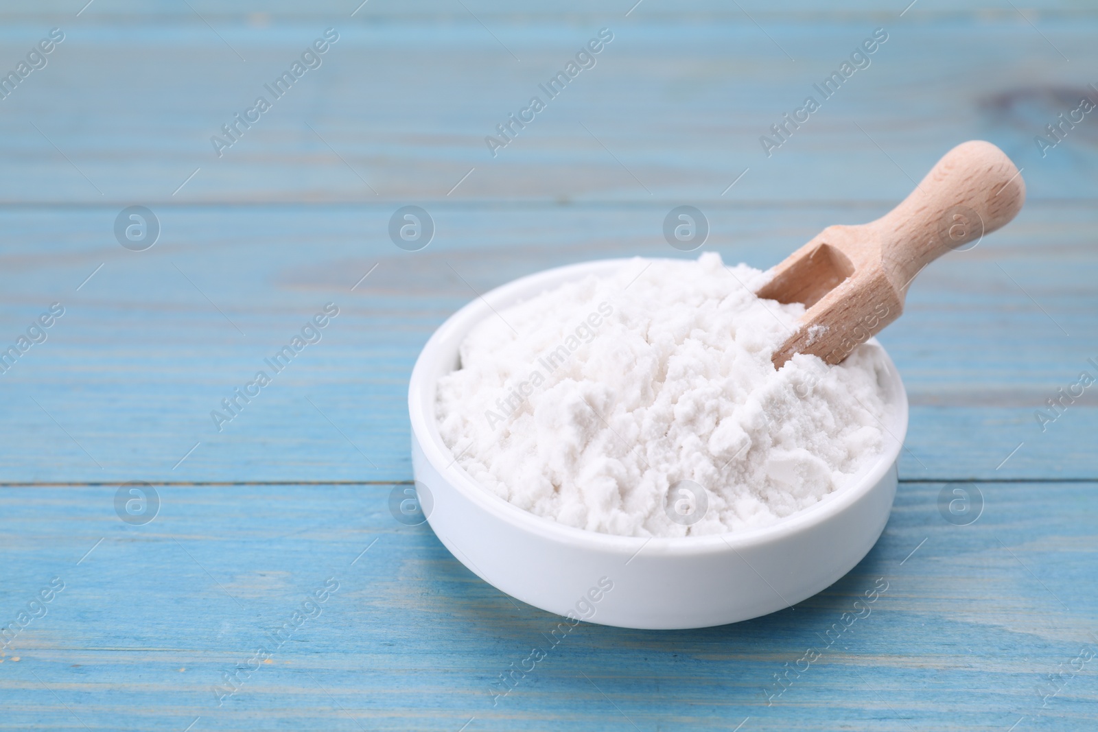 Photo of Bowl and scoop of natural starch on light blue wooden table, closeup. Space for text