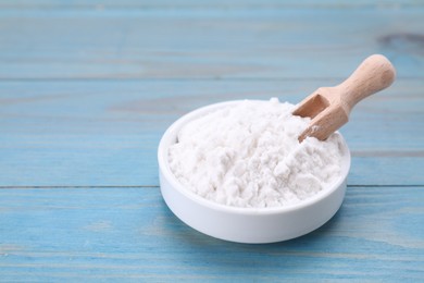 Bowl and scoop of natural starch on light blue wooden table, closeup. Space for text