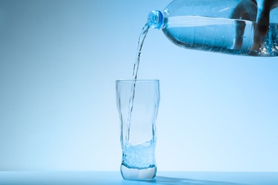 Pouring water from bottle into glass against blue background. Refreshing drink
