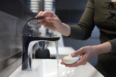 Photo of Woman with soap bar washing hands in bathroom, closeup