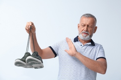 Man feeling bad smell from shoes on white background. Air freshener