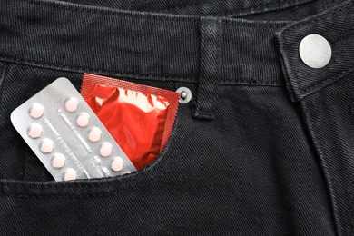 Closeup view of jeans with red condom and birth control pills in pocket. Safe sex concept